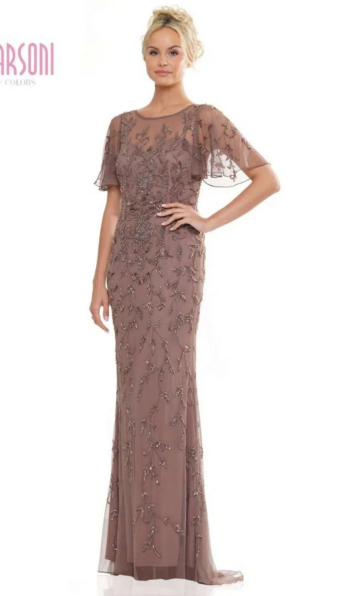 A woman models the Marsoni MV1281 long formal dress in dark taupe, featuring sheer short sleeves, intricate beadwork, and an illusion sweetheart neckline on a floor-length gown.